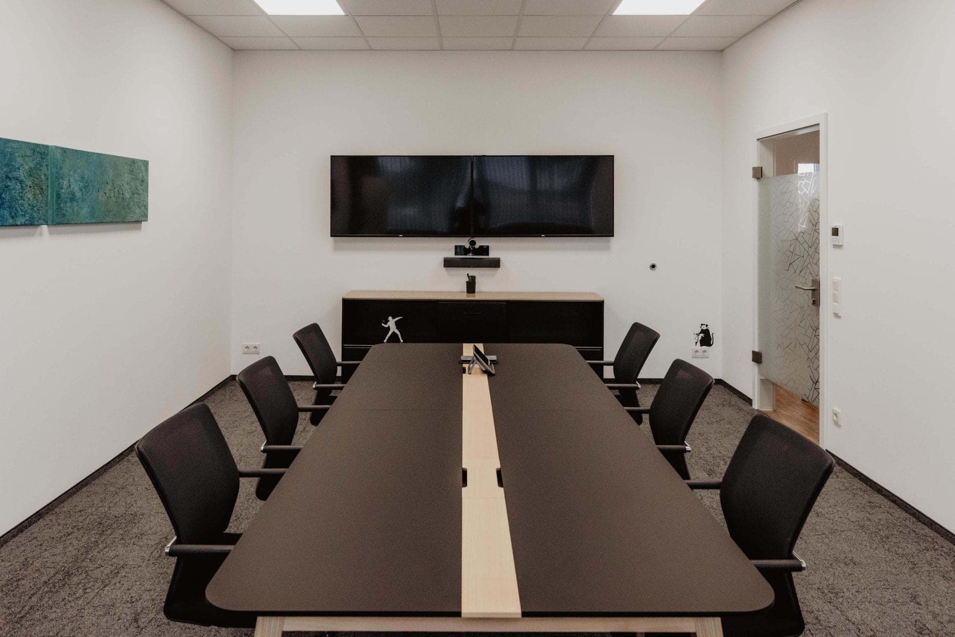 Meeting room with a dark conference table and two screens for video conferencing on the end wall