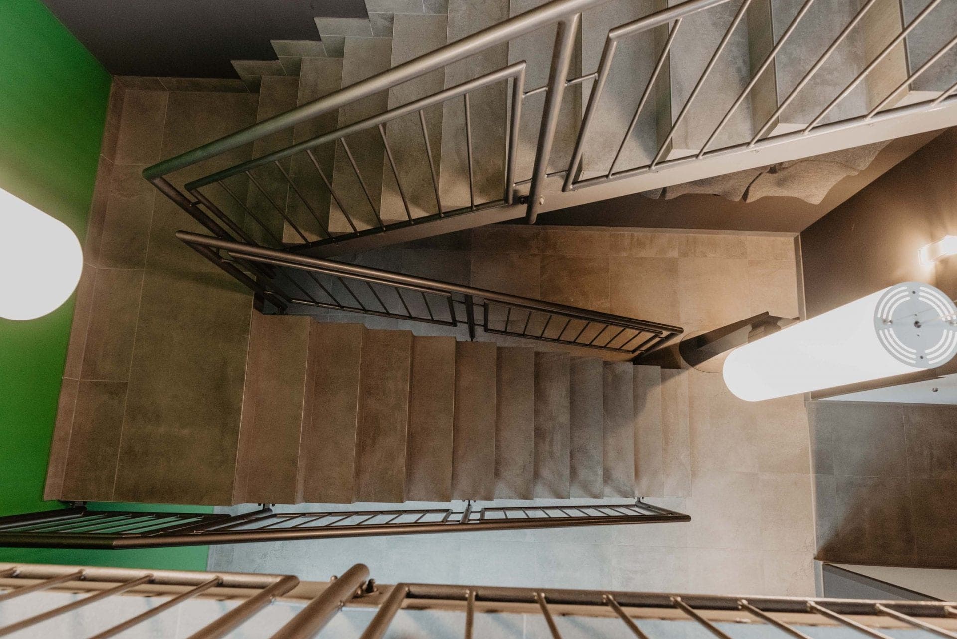 Looking down into the stairwell with tiled steps, metal railings and a green-painted wall