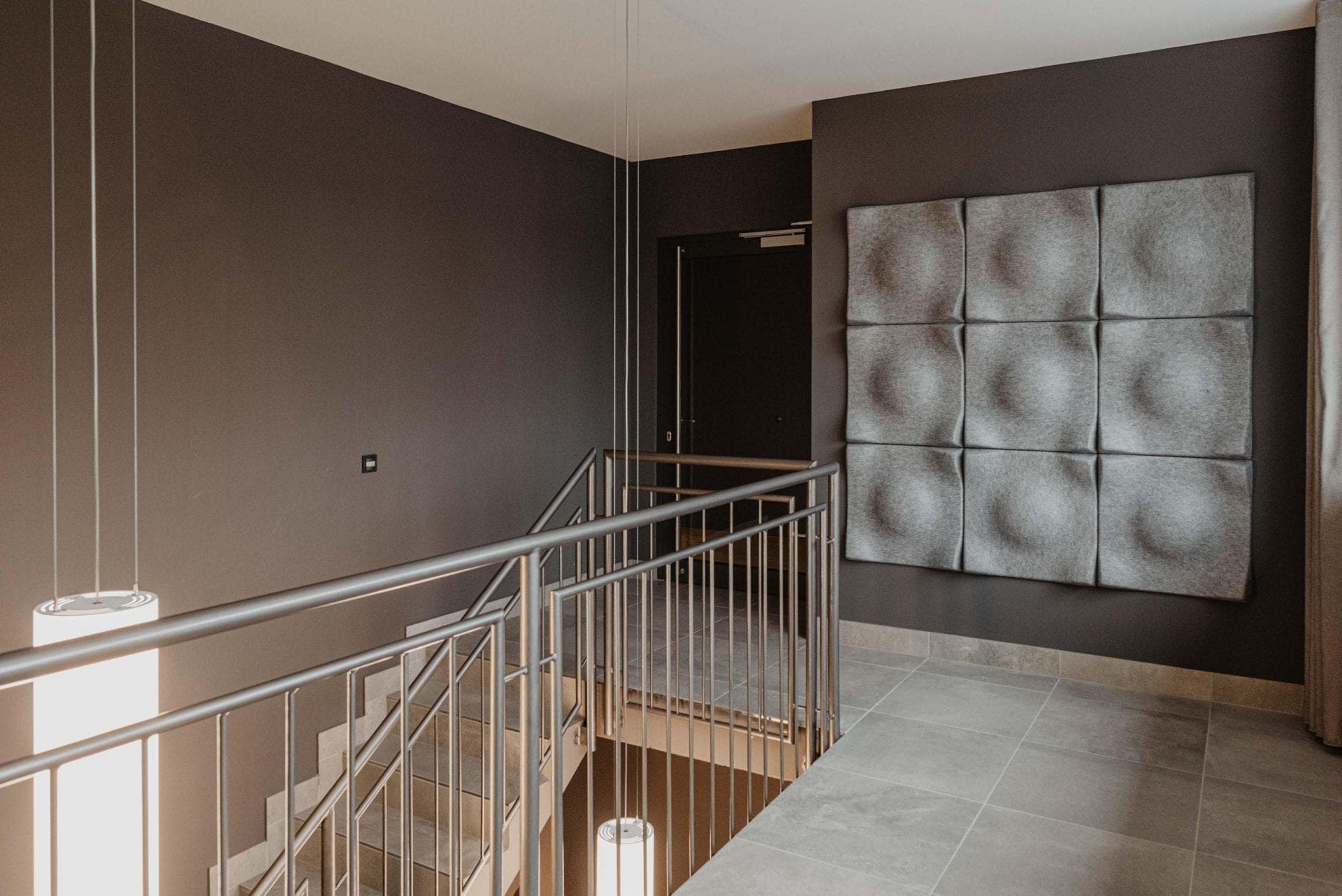 Upper floor stair landing with pendant lights and an acoustic wall of nine upholstered square panels