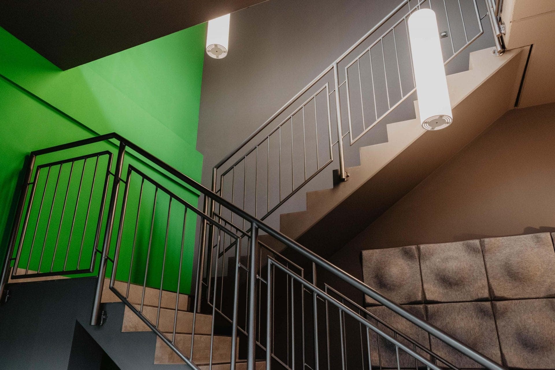 Looking up across several stair flights with a green wall surface, metal railings and acoustic panels