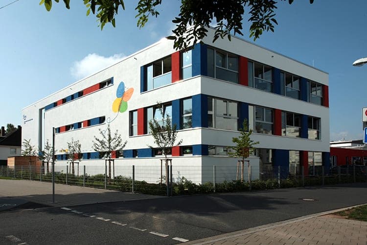 Corner view of the school from the street with a butterfly mural, fence and young trees