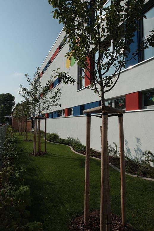 Side façade in Fürth with coloured window reveals, a strip of lawn and young trees along a planted bed