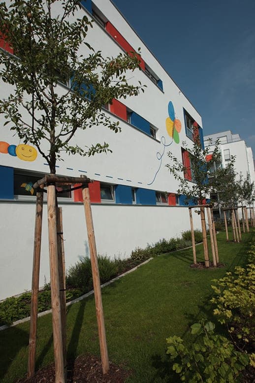 Façade with a mural of a smiling caterpillar and a colourful butterfly, young trees on the lawn in front