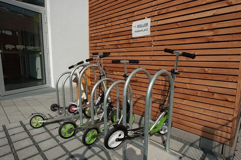 Parking for kick scooters in metal stands in front of a timber slat wall at the school entrance