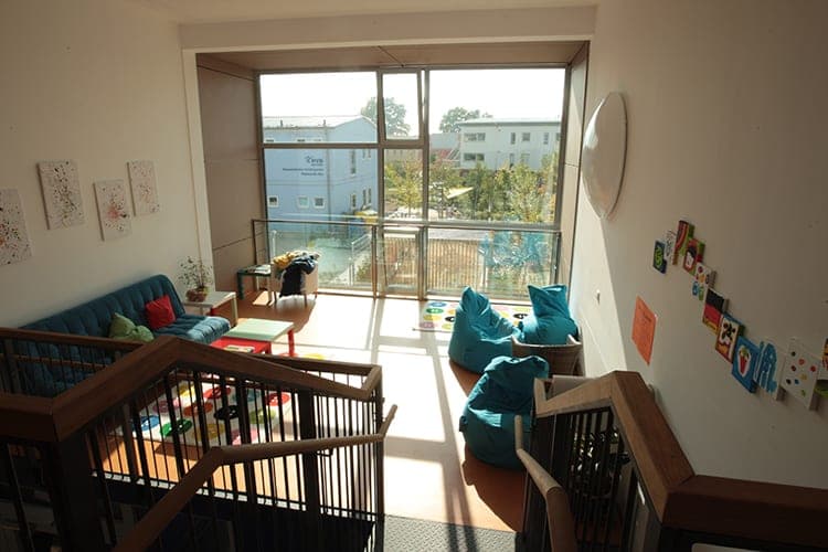 View from the stairs onto the lounge area with a sofa, bean bags and a window front with glass balustrade