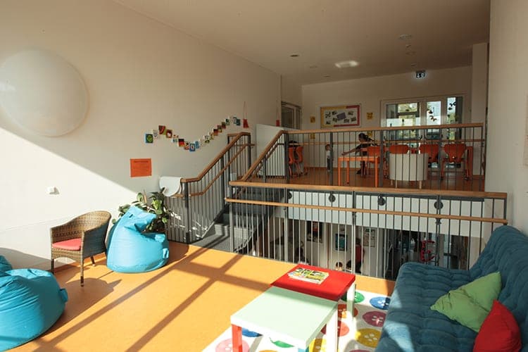 Lounge area with a sofa and bean bags, beyond it the stair opening and a raised level with tables