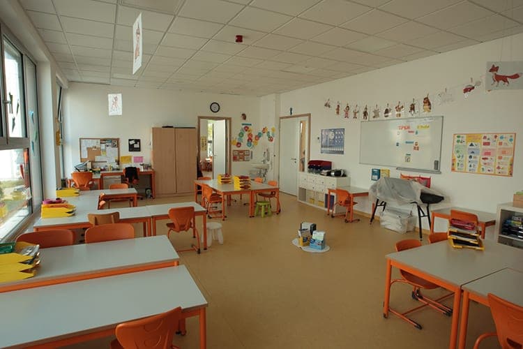 Primary school classroom with orange chairs, table groups and a whiteboard