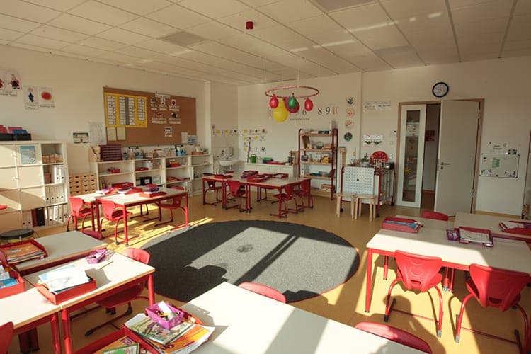 Classroom with red chairs, a round grey rug and a balloon mobile hanging from the ceiling