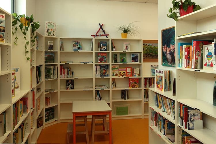 School library with white shelves full of children's books, a reading table and potted plants