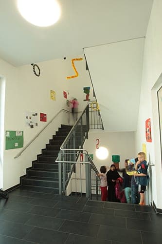 Stairwell with dark steps, children's work on the walls and pupils at the foot of the stairs