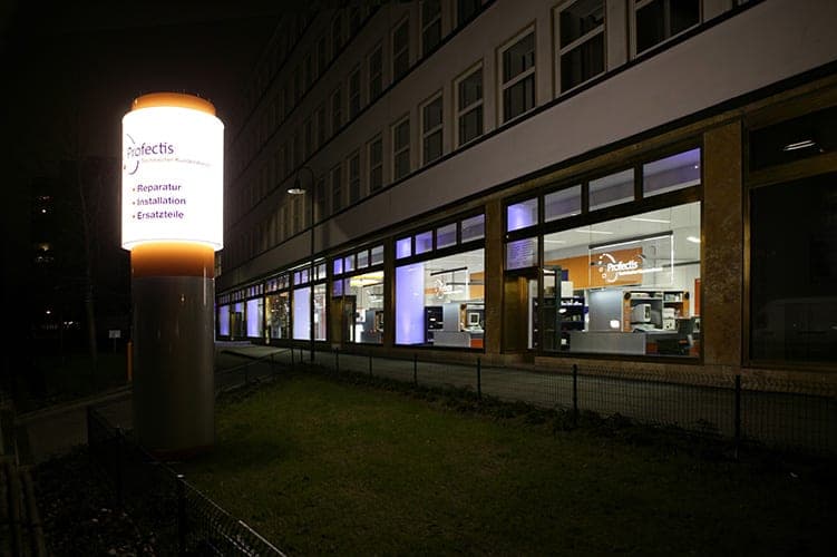Illuminated sign pylon listing services in front of the customer service centre's night-lit glazing in Berlin