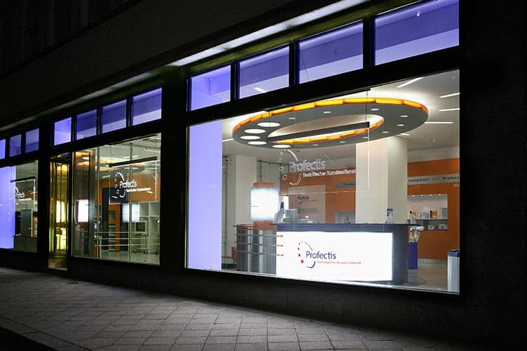 Night view through the shop windows into the reception area with its counter and orange-lit ceiling ring