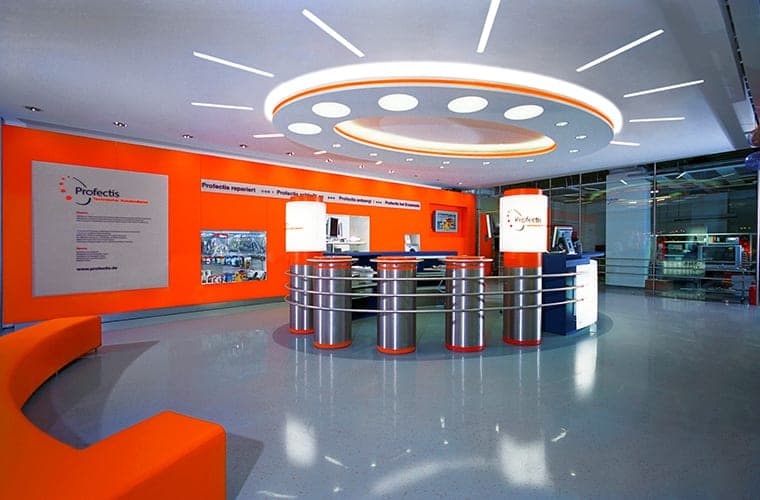 Reception area with an orange wall, circular ceiling light, a counter of steel columns and an orange bench