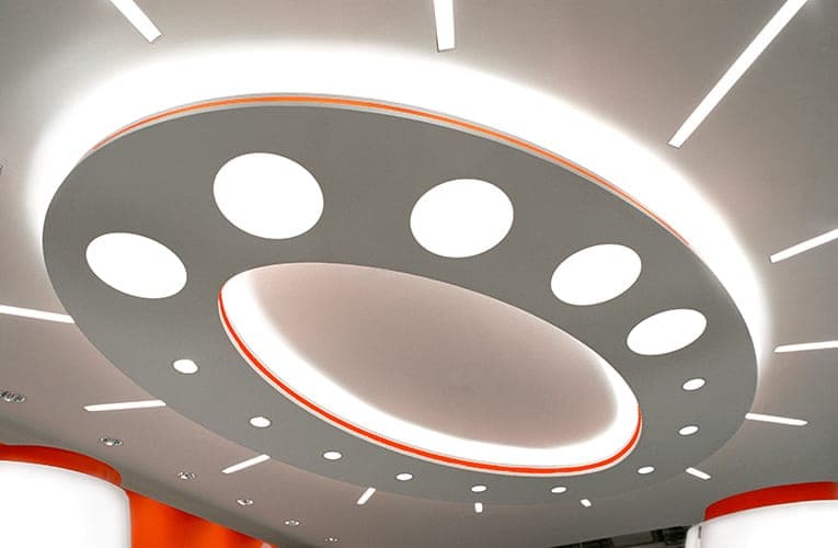 Detail of the oval ceiling light with round openings, an orange light strip and radiating linear lights