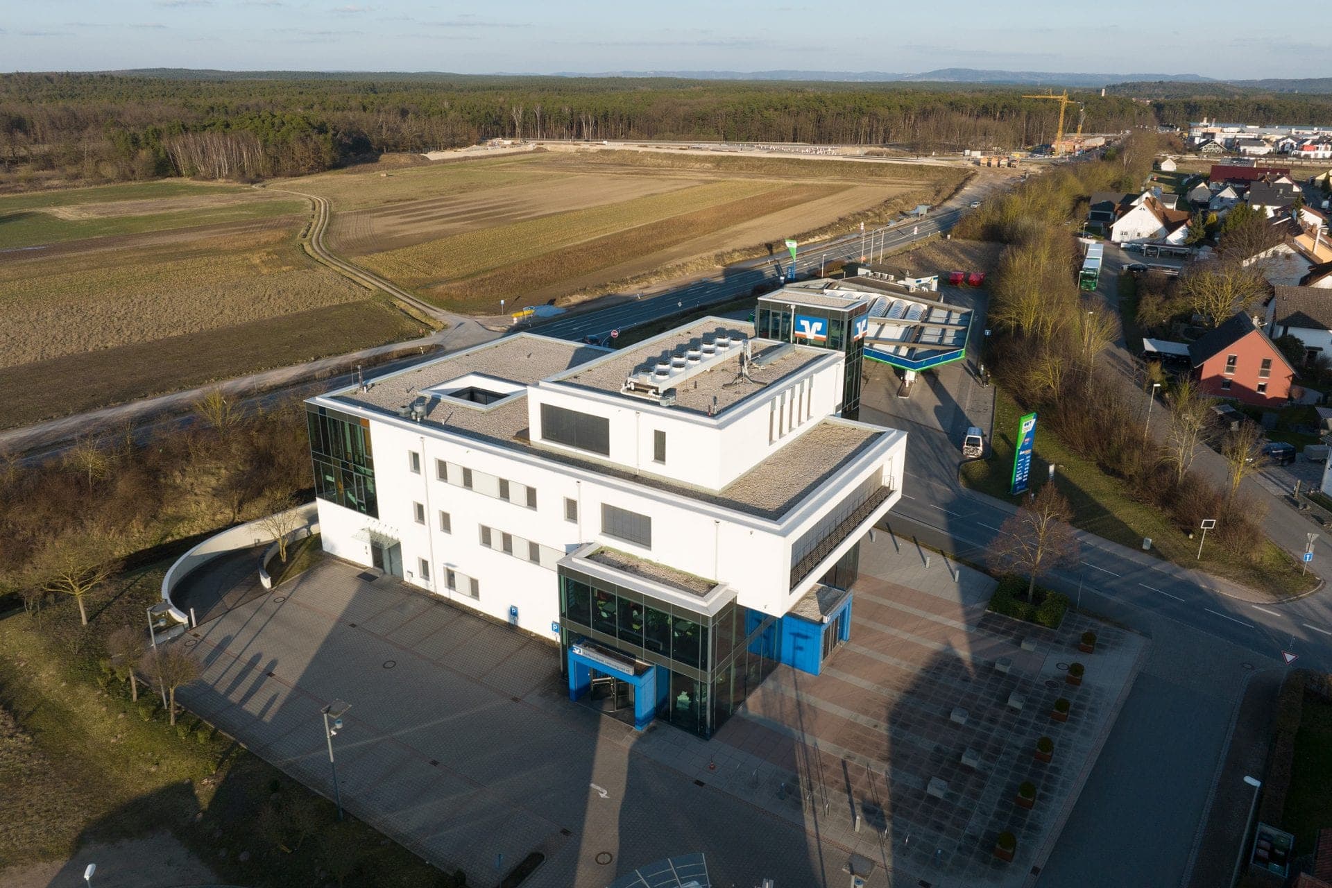 Aerial view of the bank building beside the road with fields, woodland edge and neighbouring houses