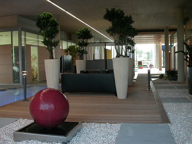 Foyer with a seating area on timber decking, tall planters and a water feature with a red sphere in gravel