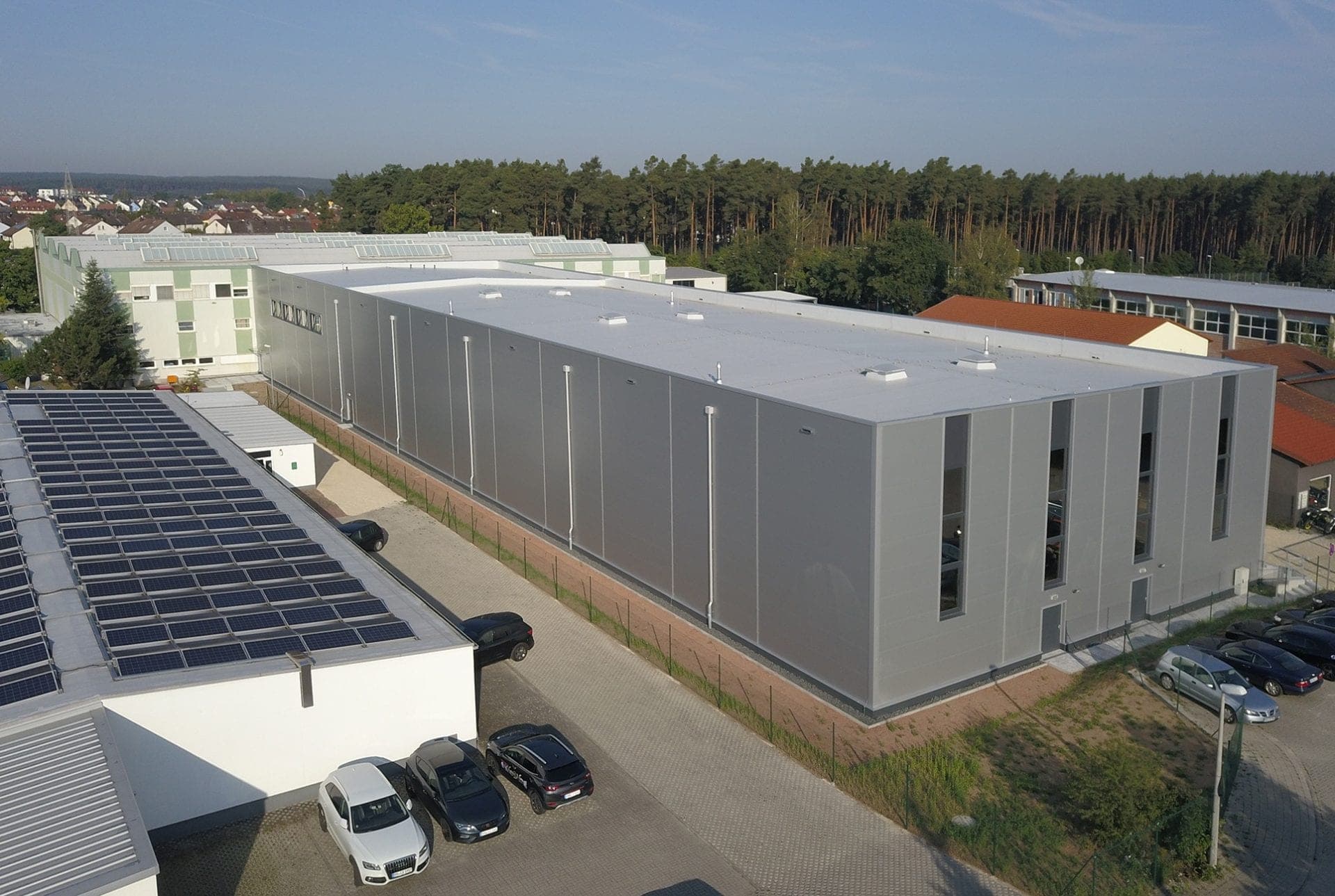 Aerial view of the high-bay warehouse with grey panel façade, narrow window slits and pine forest behind