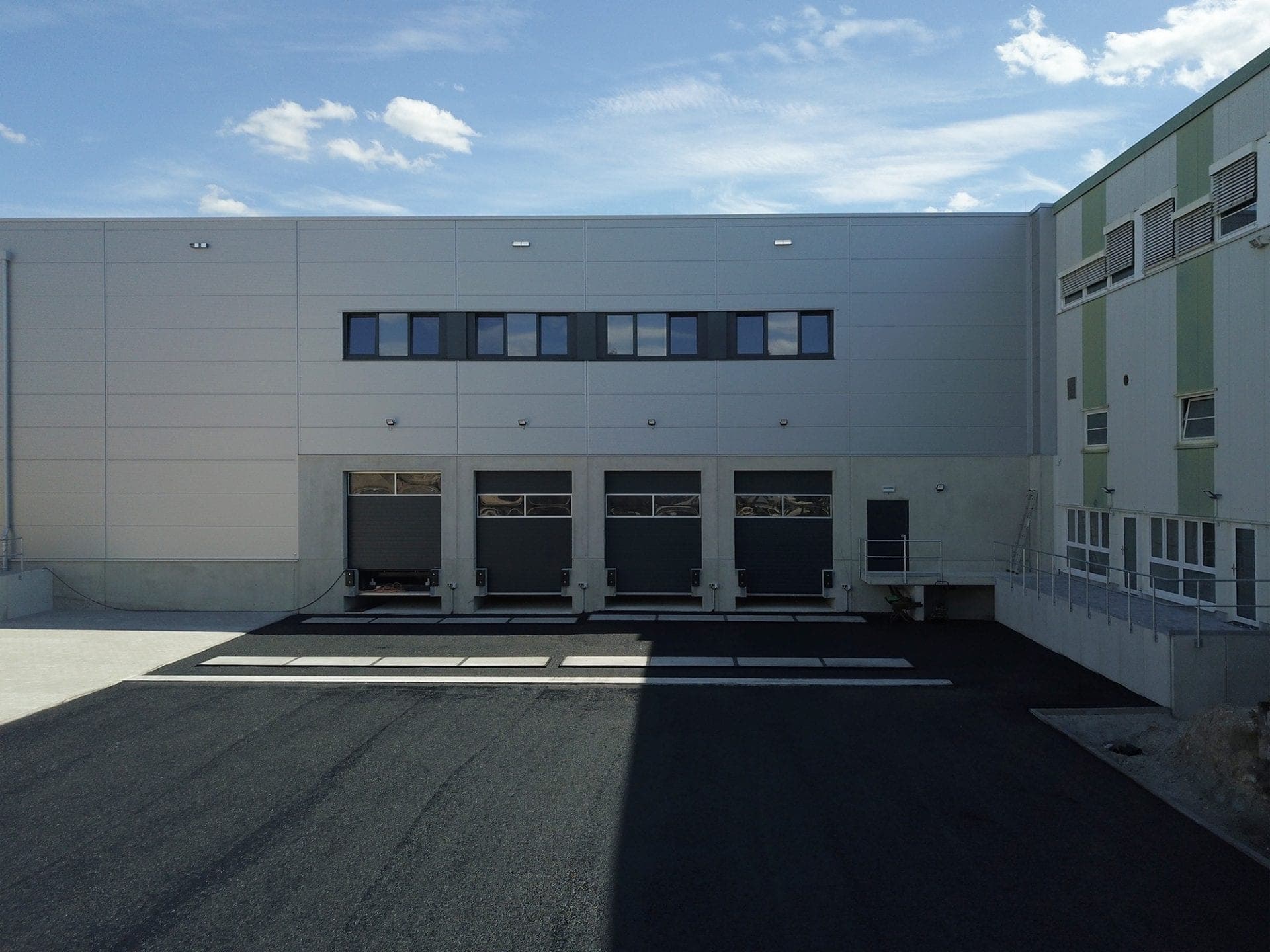 Four lorry loading docks with a strip of windows above and the adjoining existing building