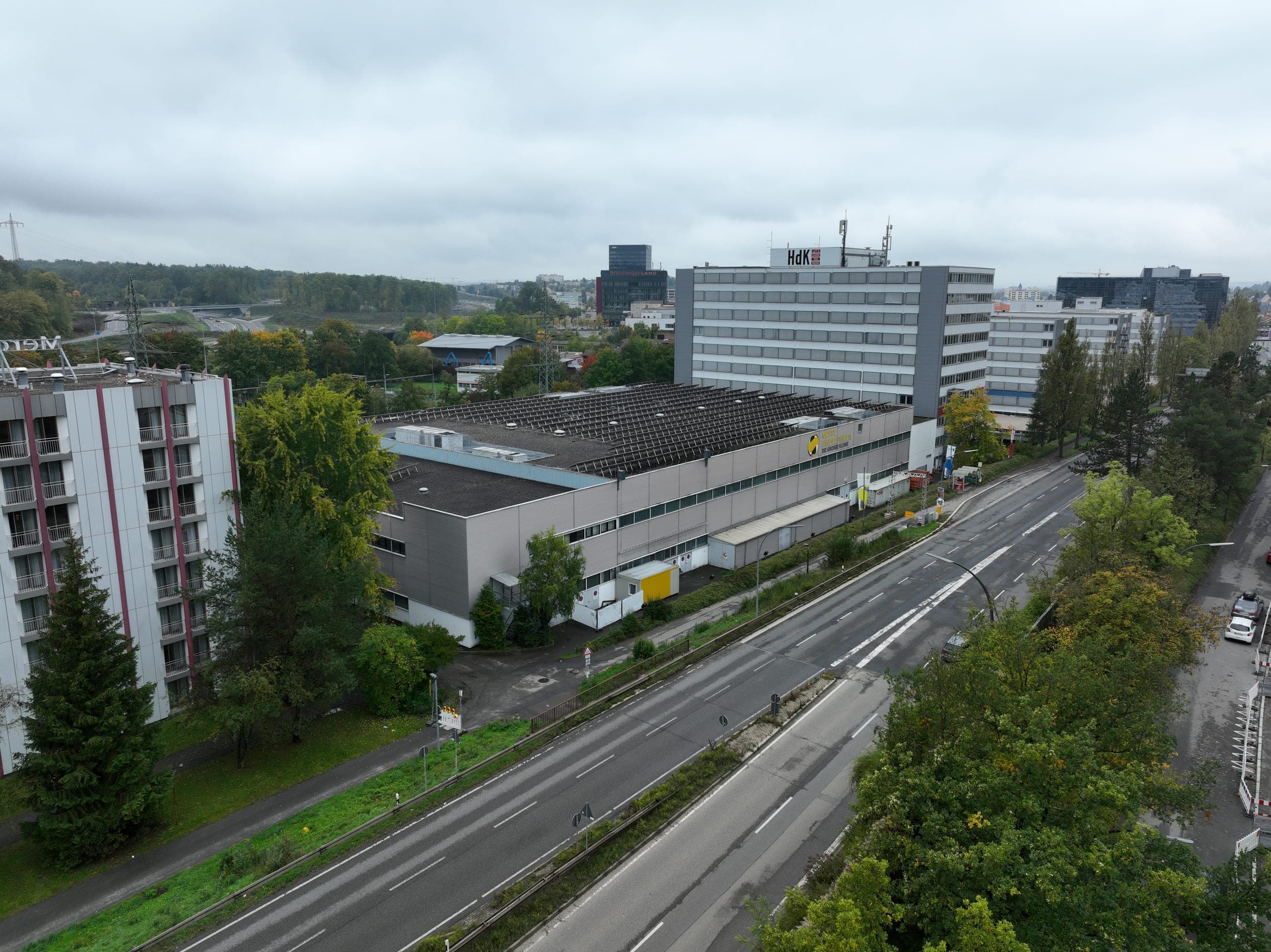 Aerial view of the former exhibition hall before conversion, with photovoltaics on the roof and high-rises behind