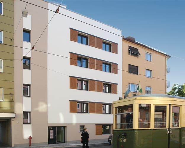 Street view of the new building with timber shutters between its neighbours, a heritage tram in the foreground
