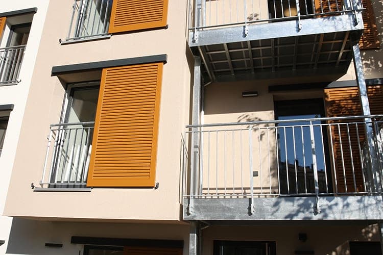 Section of the façade with orange louvred shutters, French windows and galvanised steel balconies
