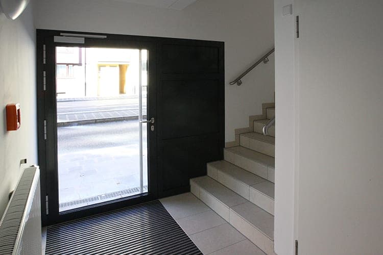Entrance hall with a staircase, a doormat grille and a view through the glazed door to the street