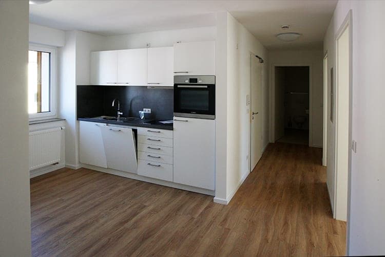 Kitchenette in a shared flat with a dark worktop and a view along the hallway to the rooms