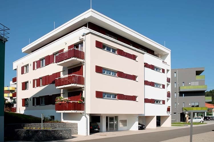 White rendered façade with red folding shutters, balconies and open parking spaces at street level