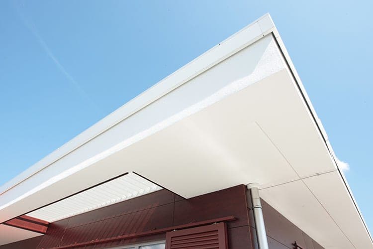 Upward view of the cantilevered roof overhang with a downpipe above the dark red shutters