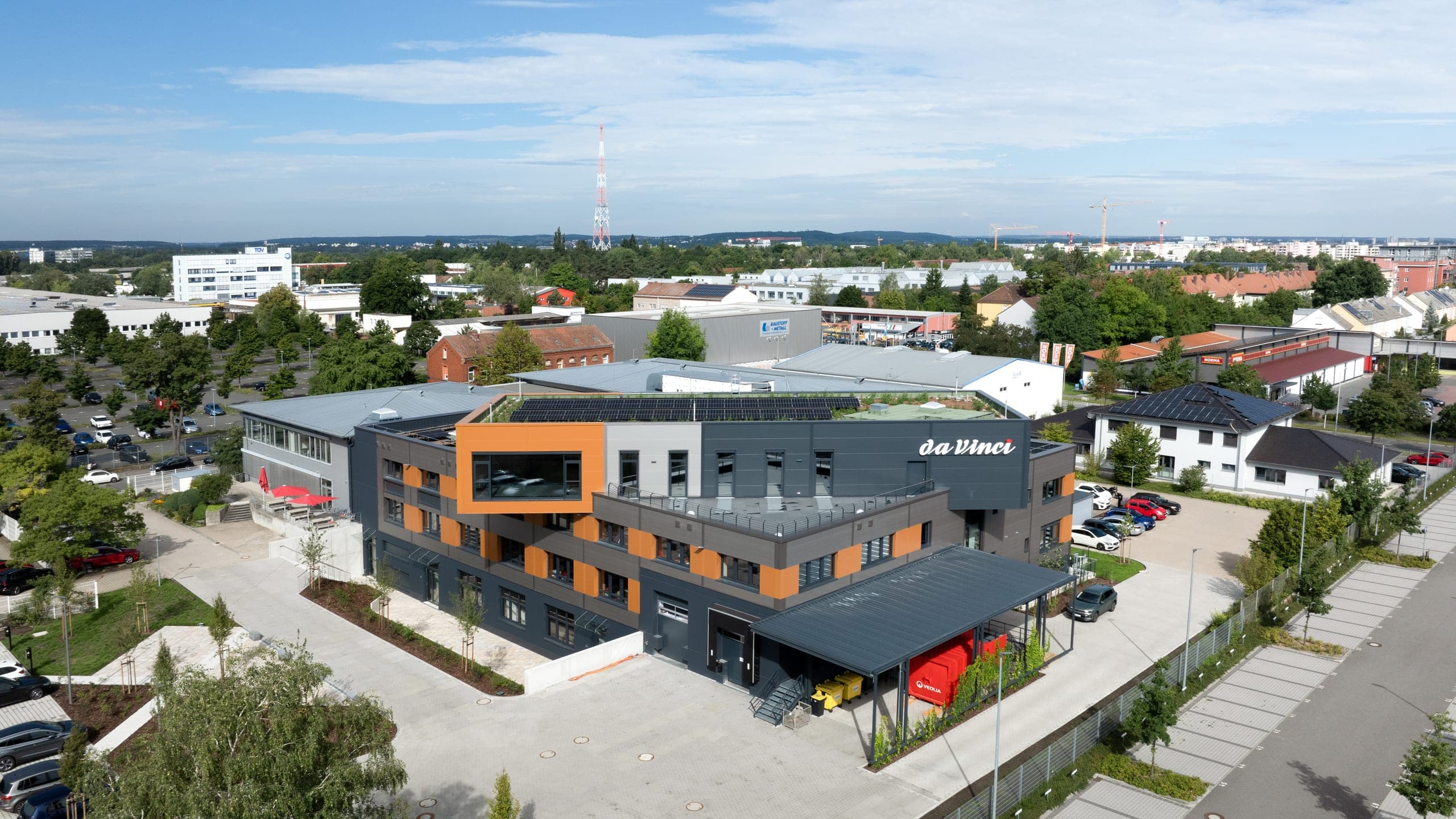 Production hall for daVinci in Nuremberg, aerial view with the orange cantilevered volume and photovoltaics on the green roof